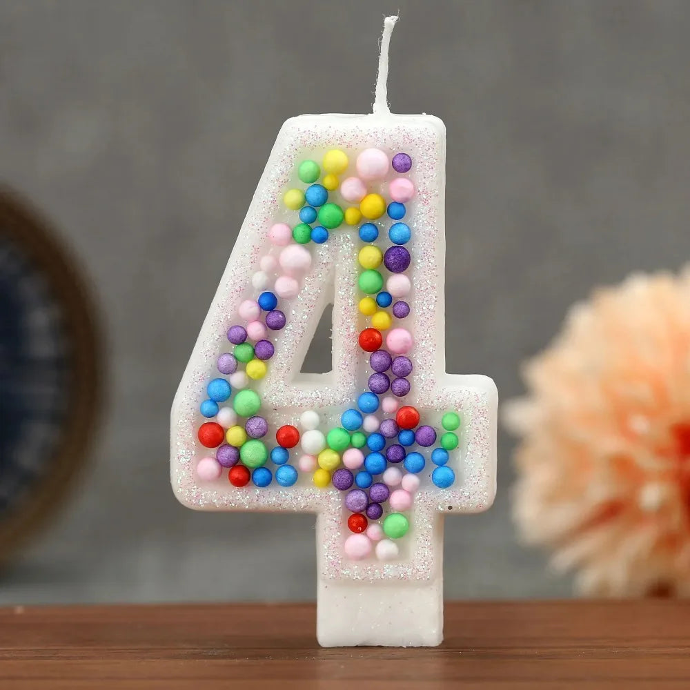 A white birthday candle shaped like the number 4 decorated with colorful candy beads
