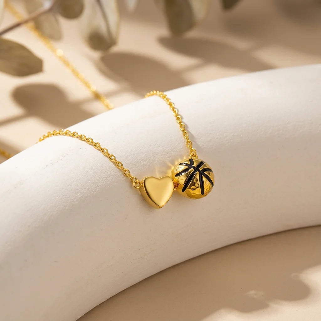 Gold heart and basketball pendant necklace resting on a light surface with soft shadows