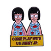 Enamel pin badge featuring two cartoon characters with black hair and glasses, with the text Come Play With Us Jimmy Jr