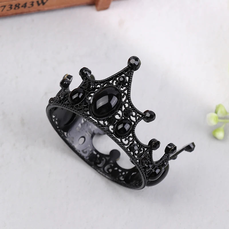 A black metal crown tiara with decorative stones and a pin, displayed on a white surface.