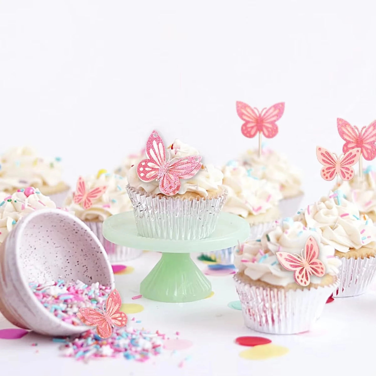 A collection of pink butterfly cake toppers decorating cupcakes and muffins on a white background.