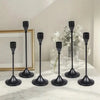 A set of black minimalist candle holders with tall slender stems and round bases displayed on a white marble surface.