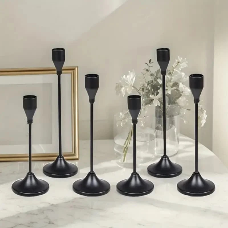 A set of black minimalist candle holders with tall slender stems and round bases displayed on a white marble surface.