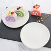 Three colorful rolled desserts on white plates and a dark slate board.