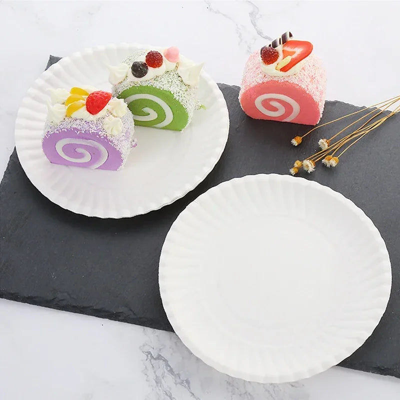 Three colorful rolled desserts on white plates and a dark slate board.