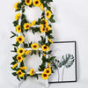 A white wooden garland decorated with yellow silk sunflowers and green leaves.