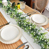 A white ceramic plate set is decorated with a green eucalyptus vine garland on a wooden table.