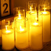 A collection of glowing candles in glass holders with flickering flames, set against a dark background.