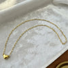 A delicate gold-colored chain necklace with a heart pendant displayed on a white velvet cloth.