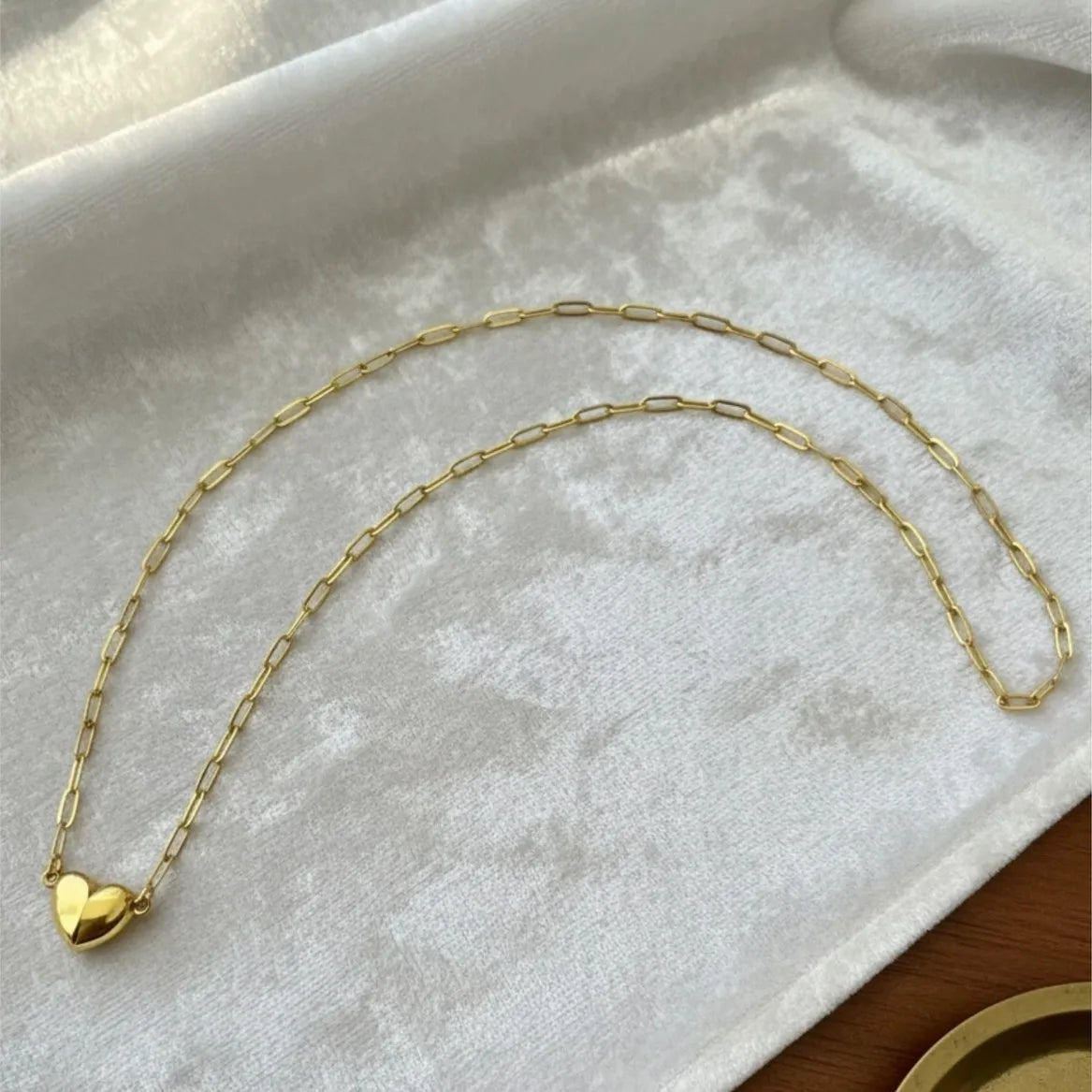 A delicate gold-colored chain necklace with a heart pendant displayed on a white velvet cloth.