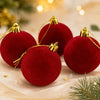 Three deep red velvet flocked Christmas ball ornaments with gold ribbons and glitter on a light background.