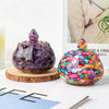 A dark purple crystal bowl with a pointed top sits next to a colorful glass bowl filled with small, sparkling stones.