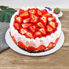 A round cake topped with fresh strawberries and cream, presented on a white plate.