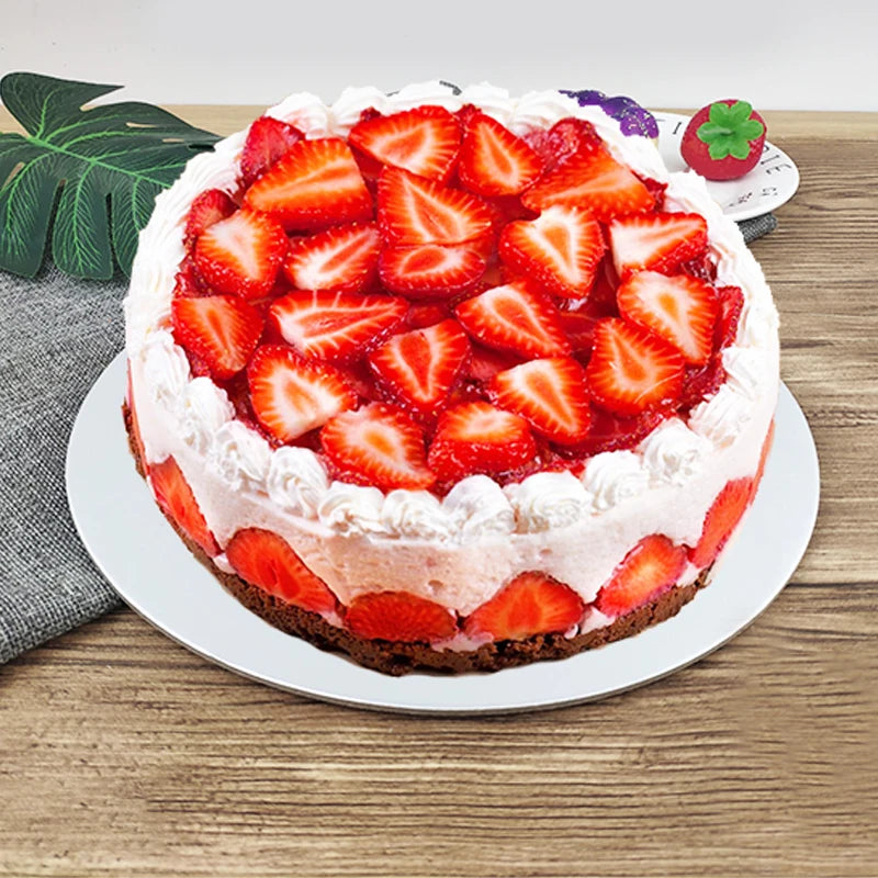 A round cake topped with fresh strawberries and cream, presented on a white plate.