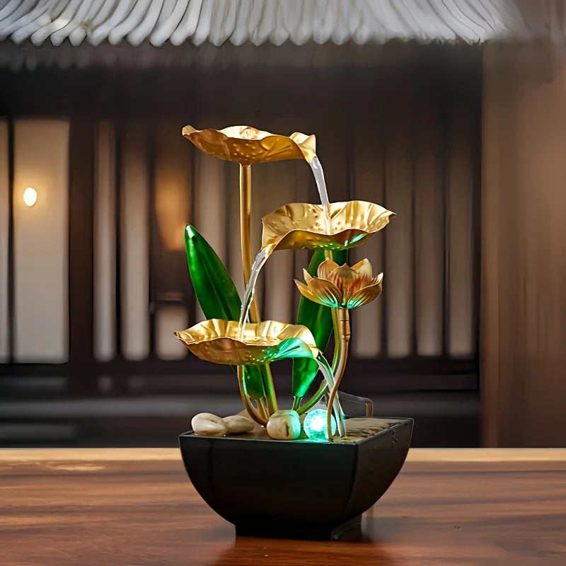 A golden plant-like fountain with green leaves and water is displayed in a black bowl on a wooden table.
