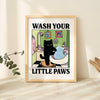 A framed poster titled Wash Your Little Paws depicting a black cat bathing in a bathtub with various bath items.