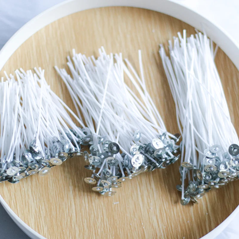 A collection of white cotton candle wicks with metal tips arranged on a light wooden surface.