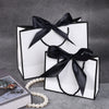 A set of elegant black and white gift bags tied with black ribbon bows displayed on a gray surface.