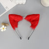 A pair of bright red plush fox ears headband with black strings and a small white flower nearby.