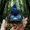 Handmade resin orgonite pyramid with natural obsidian and copper coil held against a forest background