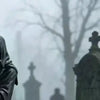 Silhouette einer gotischen Grim Reaper Statue in nebligem Freien mit kahlen Bäumen und Steinmonumenten.