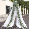White fabric draped with a green eucalyptus leaf garland in an outdoor setting.