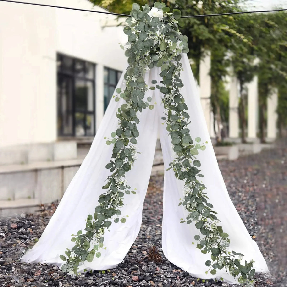 White fabric draped with a green eucalyptus leaf garland in an outdoor setting.
