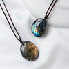 A dark, polished labradorite gemstone pendant on a brown leather cord, displayed on a white background.