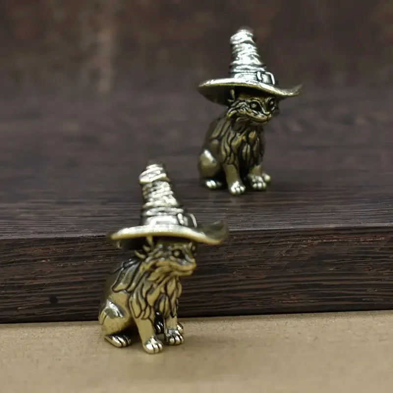 Vintage brass cat statue wearing a witch hat sitting on a dark wooden surface.