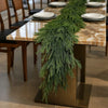 An artificial Norfolk pine Christmas garland draped across a wooden table setting.