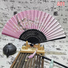 A pink and black folding hand fan displayed on a wooden stand with bamboo sticks.