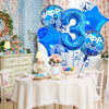 A table set for a birthday celebration featuring a white tablecloth, pink and gold decorations, and blue foil balloons.