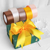 Une boîte cadeau emballée dans du papier vert avec un nœud de ruban satiné jaune et un rouleau de rubans décoratifs rose et o