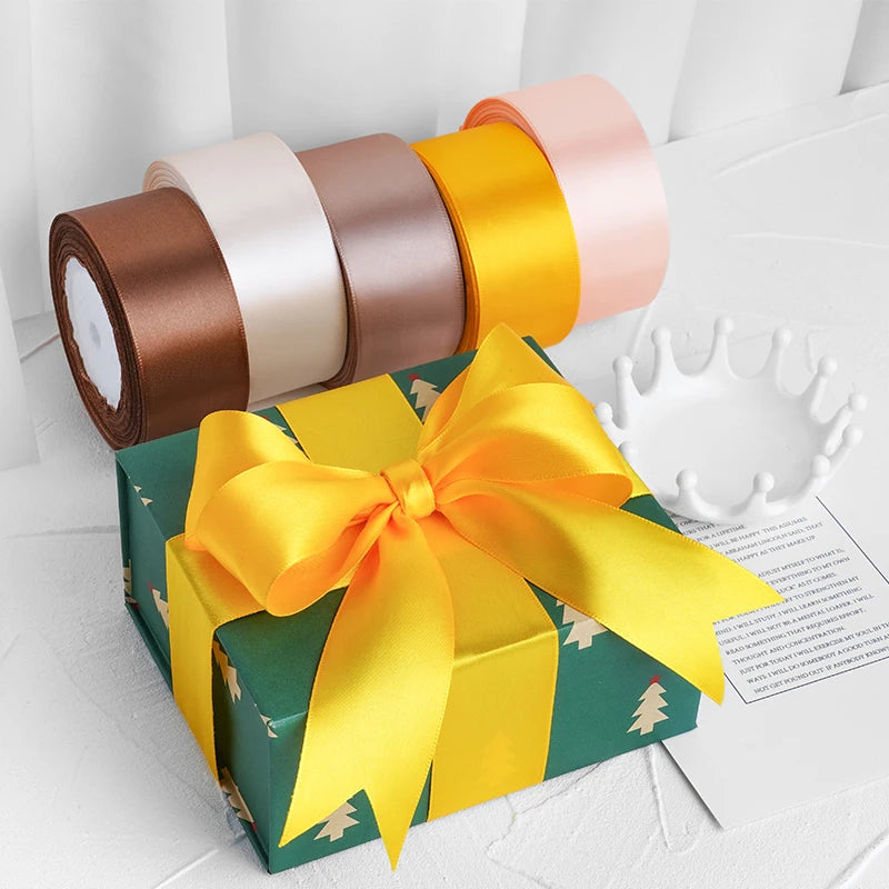 Une boîte cadeau emballée dans du papier vert avec un nœud de ruban satiné jaune et un rouleau de rubans décoratifs rose et o