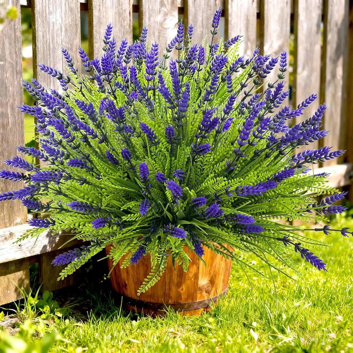 A vibrant bouquet of artificial purple lavender flowers in a wooden pot set against a green lawn.