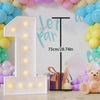 A large white LED marquee number one balloon frame decorated with pastel balloons and a purple gift box.