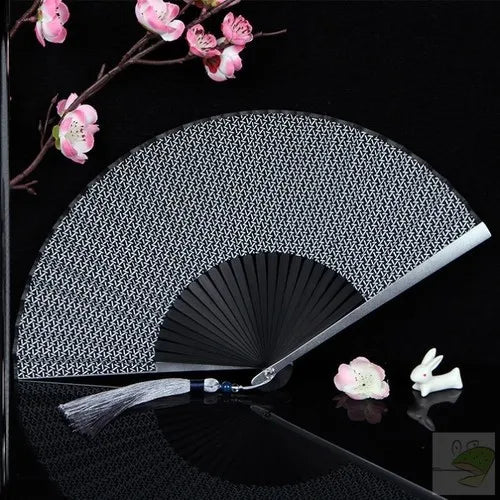 A silver titanium alloy folding hand fan with a textured surface and white floral accents is displayed on a black background.