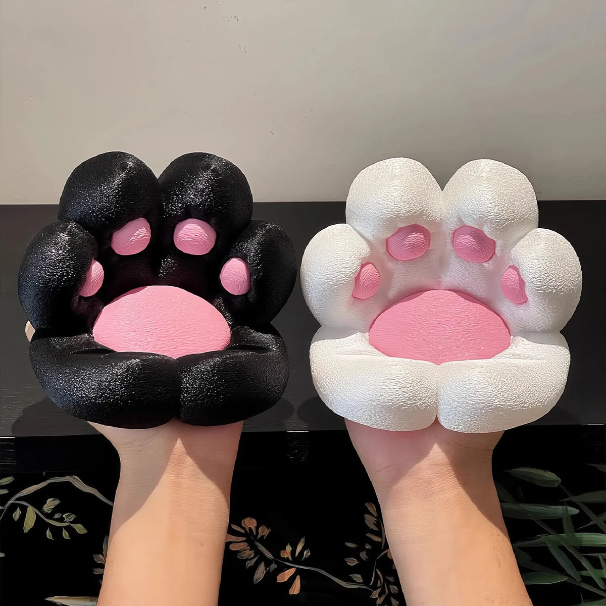 A pair of hands holds a black and pink cat paw silicone phone stand with a stress relief design.