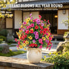 A vibrant bouquet of mixed artificial violet flowers in various shades of pink, purple, and yellow displayed in a white pot.