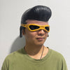 A man wearing a yellow half-face latex mask with black detailing and a dark hairstyle, posing against a white background.