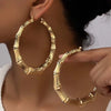 A pair of oversized bamboo hoop earrings in gold worn by a woman.