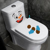 A white toilet decorated with a funny cartoon face decal featuring an orange nose and wide smile.