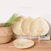 A set of peach-shaped bamboo woven hand fans displayed next to a potted green plant.