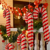 A string of red and white striped candy cane foil balloons hanging in front of a white railing decorated with festive lights.