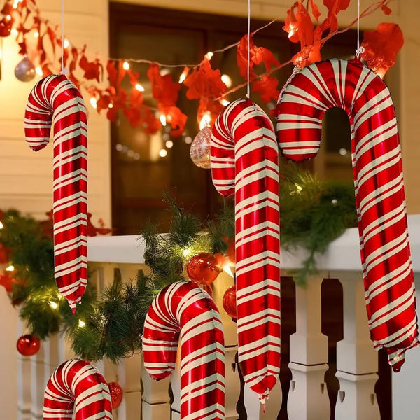 A string of red and white striped candy cane foil balloons hanging in front of a white railing decorated with festive lights.