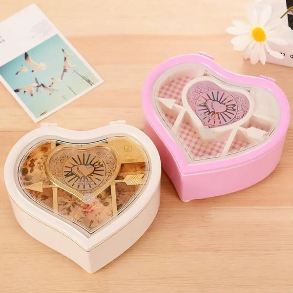 A pink heart-shaped ballerina music box with a clear lid and an open version displaying a gold heart design.