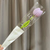A clear glass tube containing a handmade crochet tulip bouquet with purple and green flowers.
