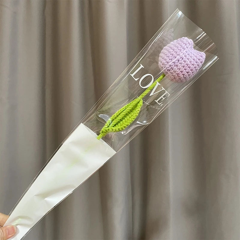 A clear glass tube containing a handmade crochet tulip bouquet with purple and green flowers.