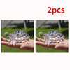 Two clear glass miniature tortoise statues being held in a hand against a green outdoor background.