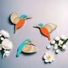 Three vintage wooden bird wall decorations in orange and teal against a light gray background with white flowers.